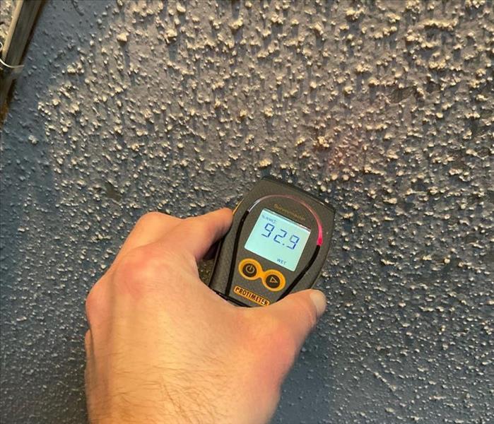 Technician assesses popcorn ceiling water damage with a moisture sensor