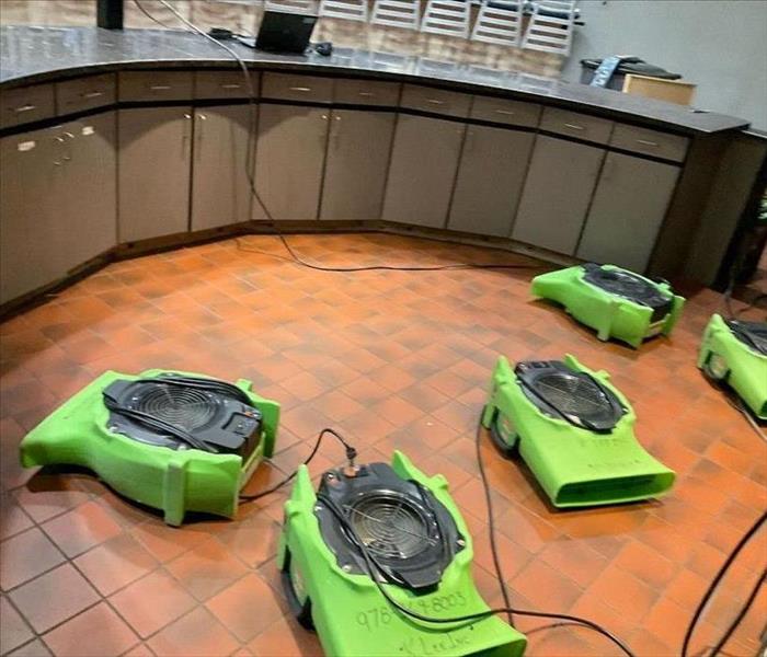 Six SERVPRO air movers and a dehumidifier operating near a semicircular counter on a tile floor